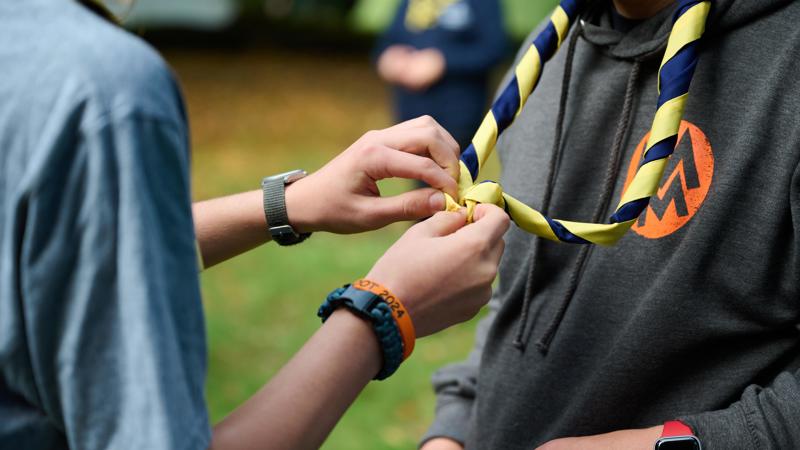 Two Scouts tying a woggle, one wearing a hoodie with the Scouts logo