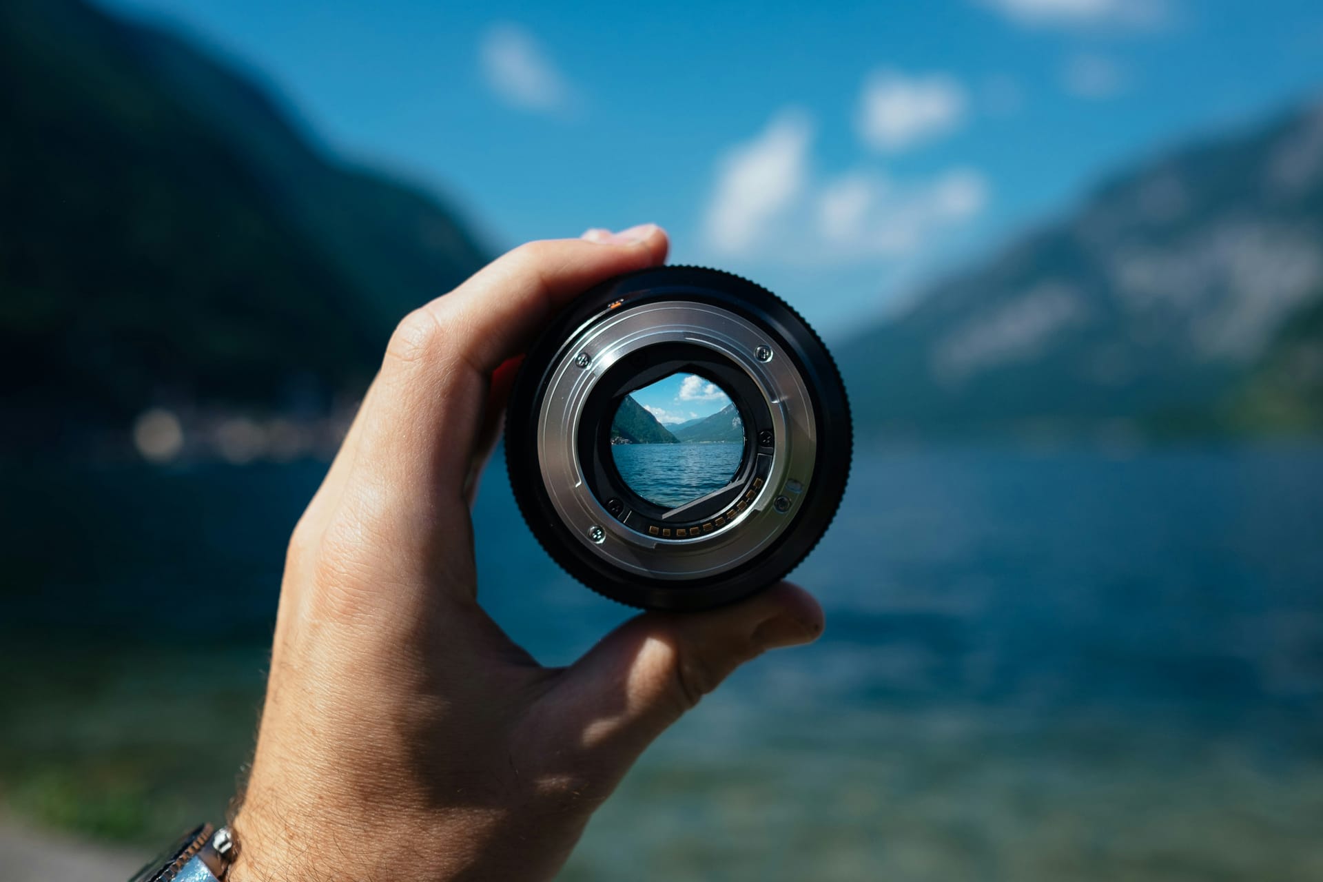 A hand holding a camera lens that brings a blurred mountain lake into sharp focus
